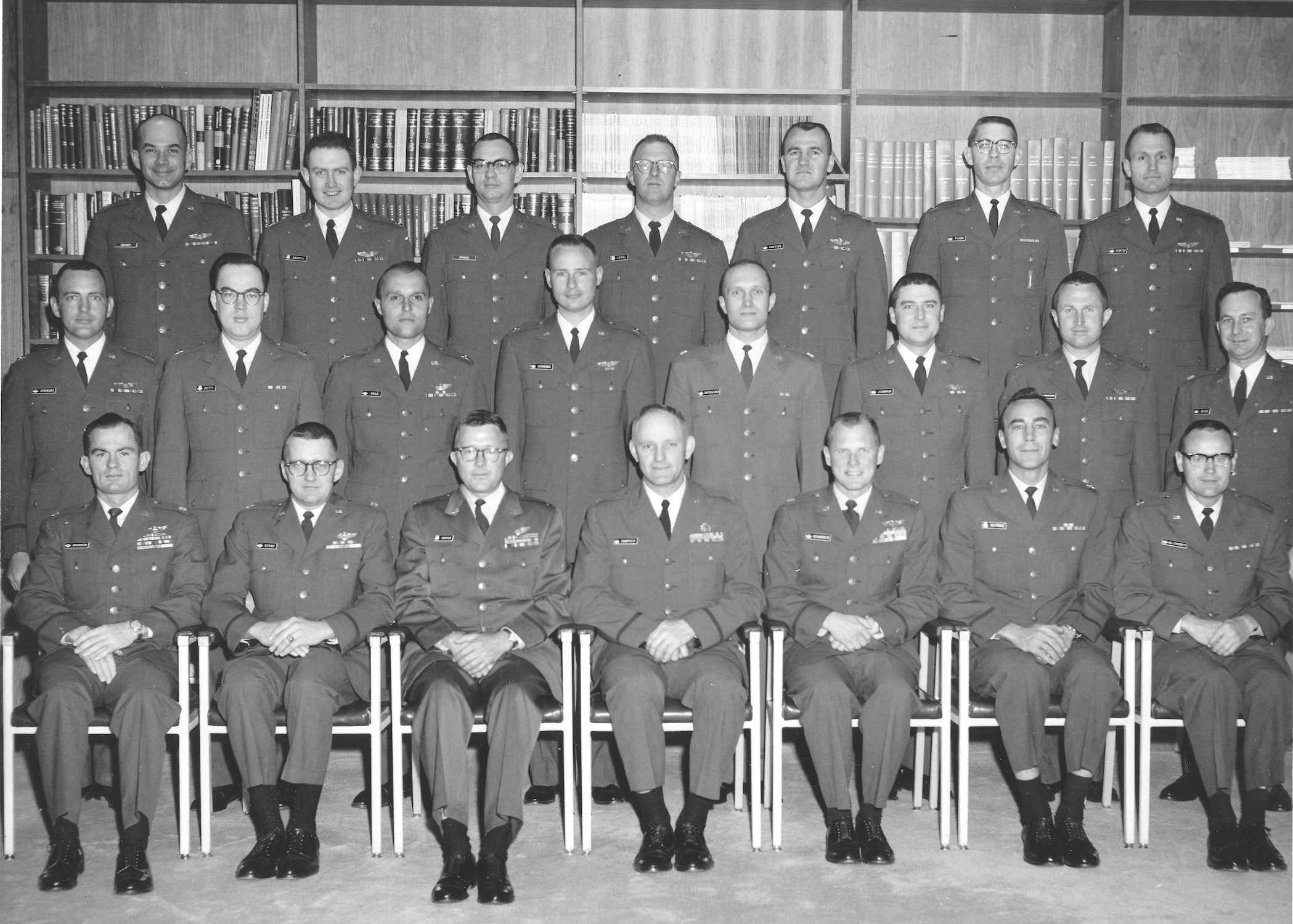 Three rows of men in Air Force uniforms and regulation haircuts are pictured. Jennings in uniform, glasses, and tie stands third from left in the back row. The front row, of 7, is seated; the two back rows of 8 and 7 respectively, are standing, with a bookcase behind them.
