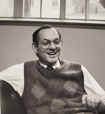 Jennings, in plaid vest, seated in his office: leaning back in his chair, laughing.