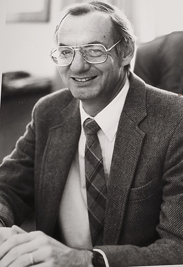 Jennings, seated, in sports jacket and tie, smiles into the camera.