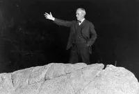 Robert A. Millikan gesturing from on top of a rock